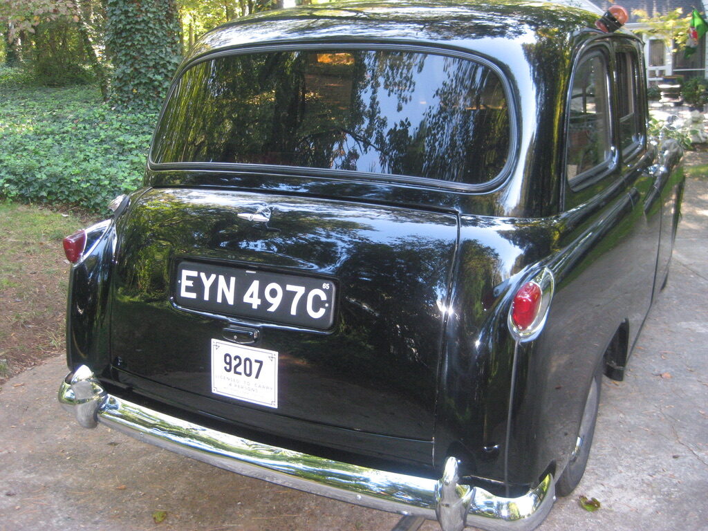The rear of the taxi in daylight, black paint polished to a mirror, London plate EYN 497C above a licence plate reading 9207.